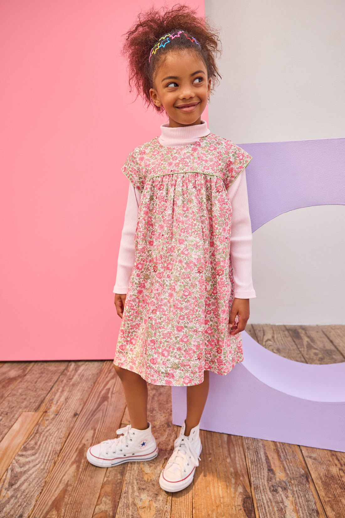 Model can be seen wearing woven short sleeve dress, with a ribbed turtleneck paired underneath to complete the look. Dress features a beautiful pink/green floral, button closure on back, and a beautiful green trim across bust and edge of sleeves for an elevated look. 