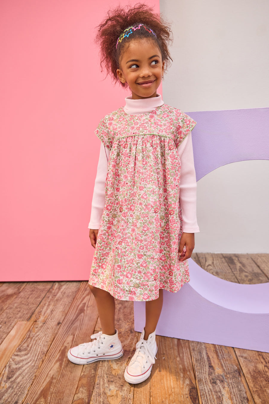 Model can be seen wearing woven short sleeve dress, with a ribbed turtleneck paired underneath to complete the look. Dress features a beautiful pink/green floral, button closure on back, and a beautiful green trim across bust and edge of sleeves for an elevated look. 