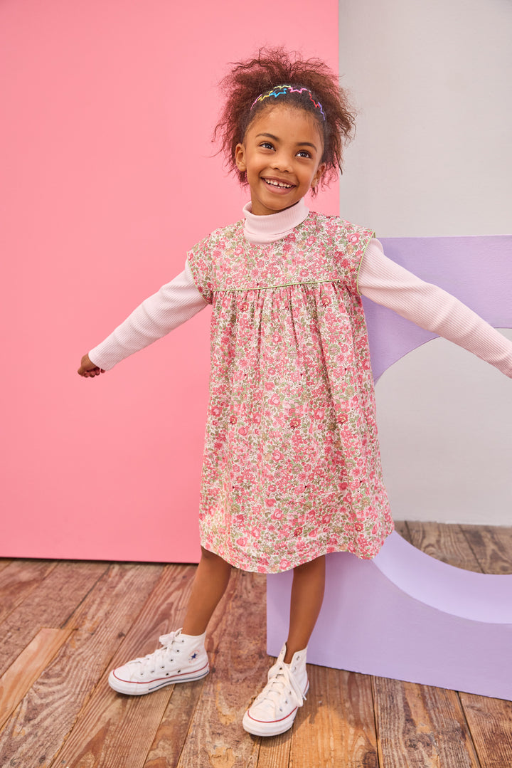 Model can be seen wearing woven short sleeve dress, with a ribbed turtleneck paired underneath to complete the look. Dress features a beautiful pink/green floral, button closure on back, and a beautiful green trim across bust and edge of sleeves for an elevated look. 