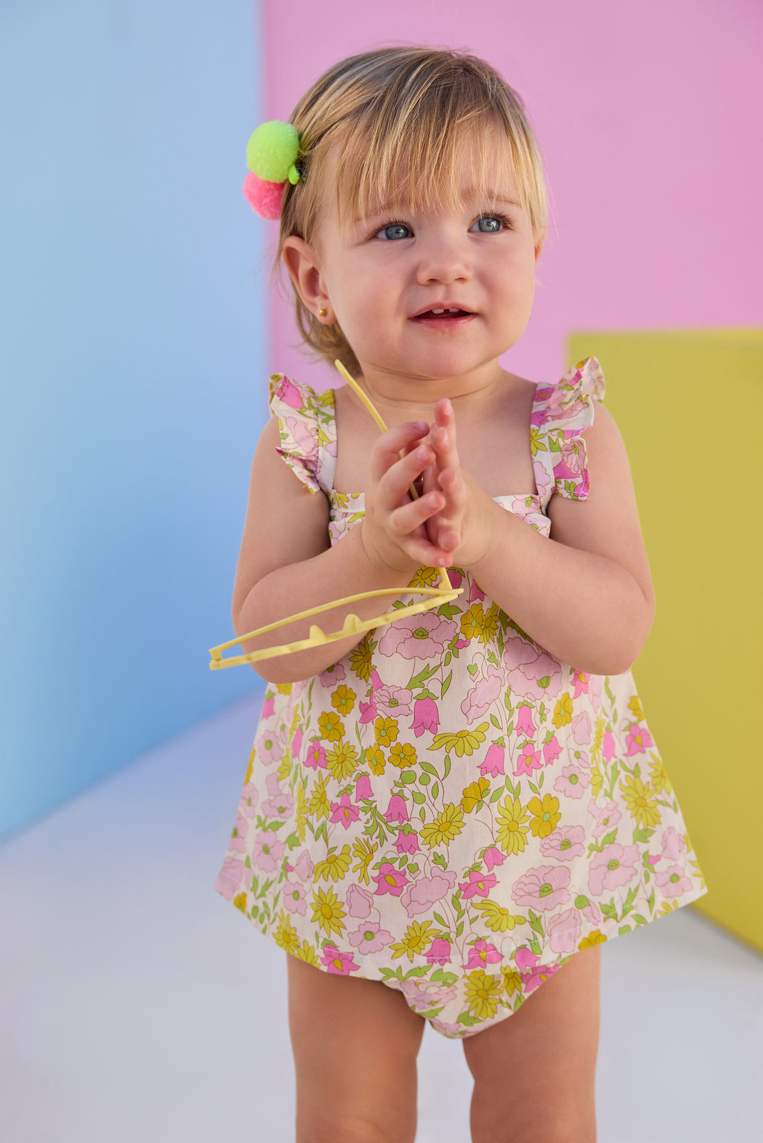 Baby model can be seen wearing a two piece woven bloomer set in a beautiful pink and yellow floral print. Top features button closure at end of straps along back, and bottoms are easy pull on style for a secure but comfy fit. 
