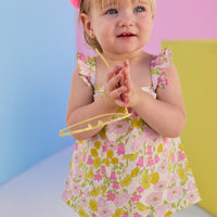 Baby model can be seen wearing a two piece woven bloomer set in a beautiful pink and yellow floral print. Top features button closure at end of straps along back, and bottoms are easy pull on style for a secure but comfy fit. 