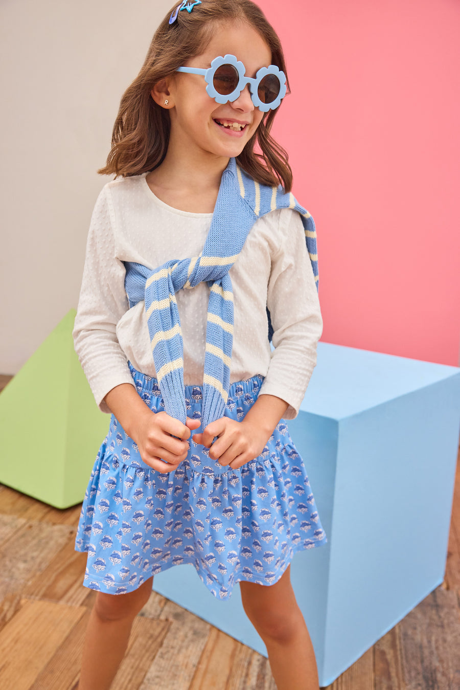 Tween model can be seen wearing a white long sleeve t-shirt paired with a knit blue floral skort with a blue and white stripe sweater tied over the shoulder to complete the look. 