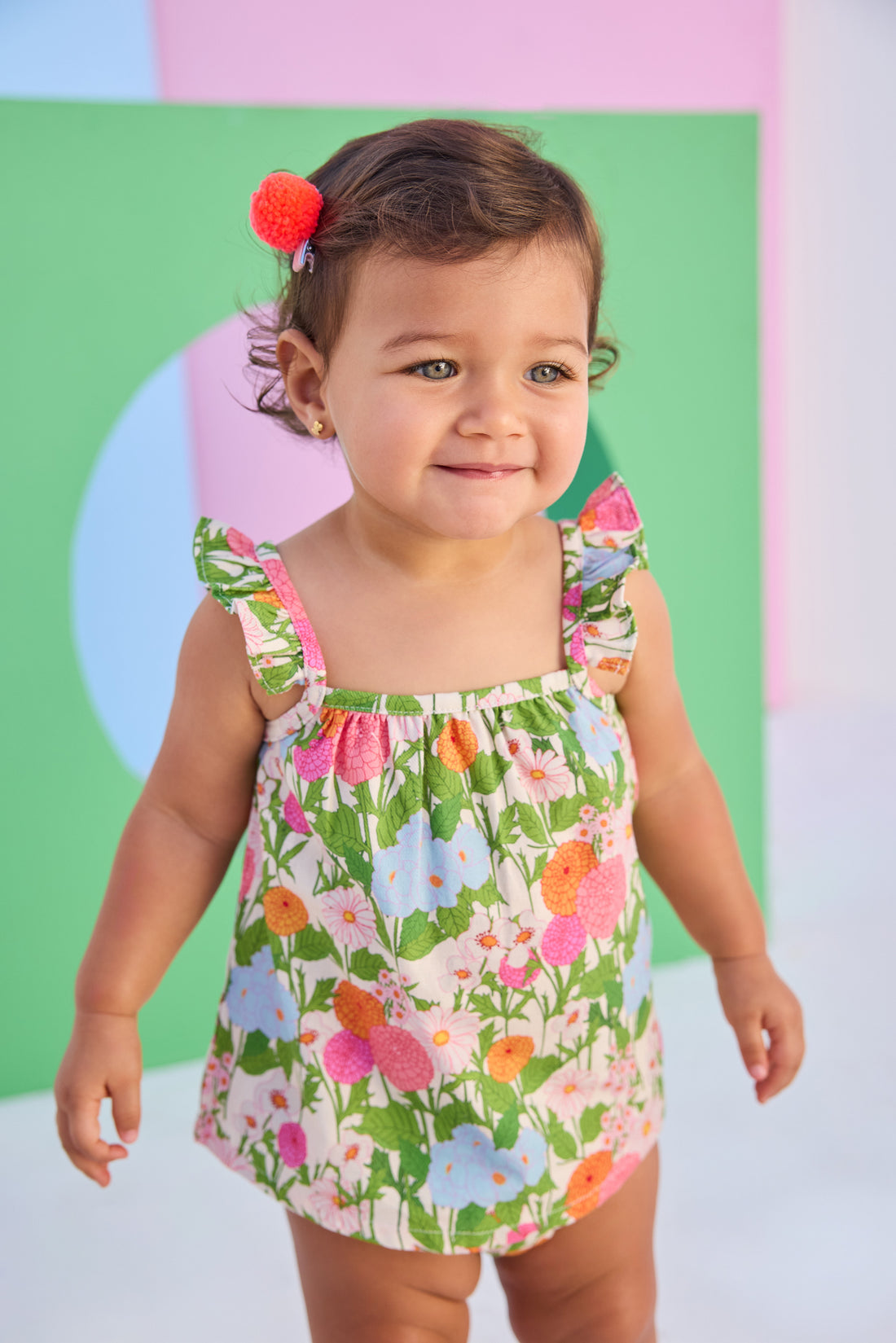 Baby model can be seen wearing a two piece woven bloomer set in a beautiful green/pink/orange/light blue floral print. Top features button closure at end of straps along back, and bottoms are easy pull on style for a secure but comfy fit. 