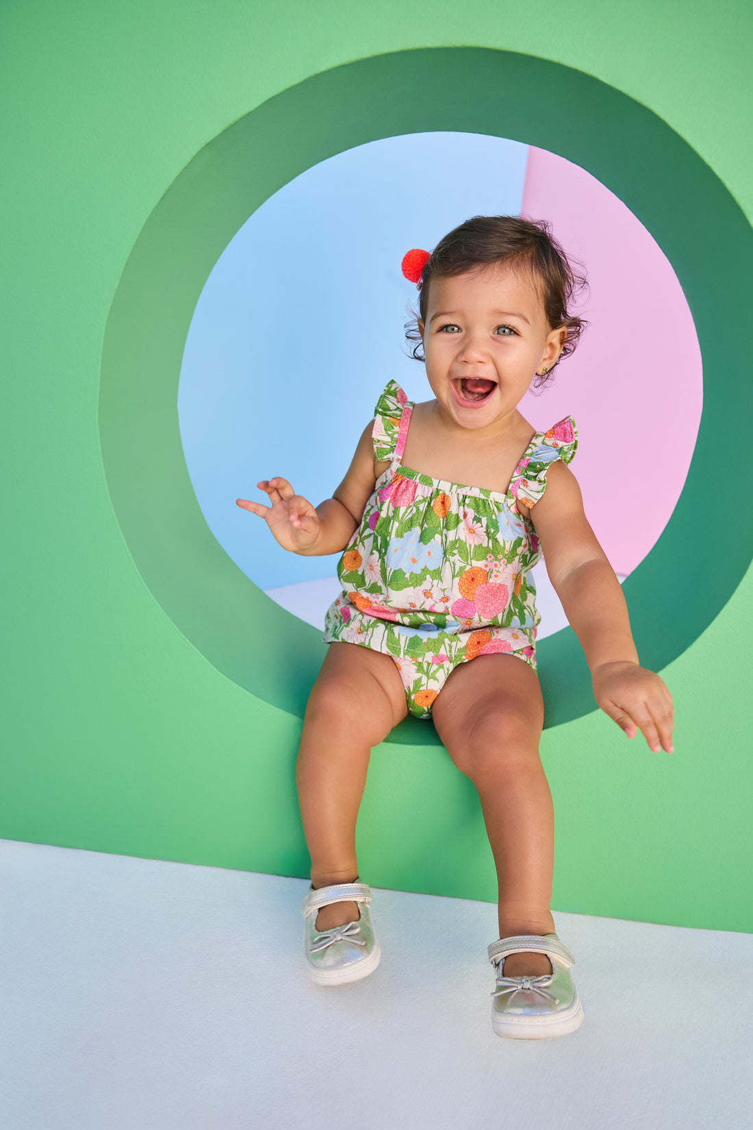 Baby model can be seen wearing a two piece woven bloomer set in a beautiful green/pink/orange/light blue floral print. Top features button closure at end of straps along back, and bottoms are easy pull on style for a secure but comfy fit. 