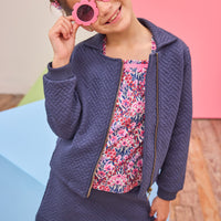 Model can be seen wearing a quilted knit jacket that features pockets on the sides and a gold zipper for an elevated look. Pair back perfectly with the matching skort in the same fabric and color and a long sleeve navy/pink/cranberry floral shirt to complete the look. 