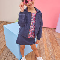 Model can be seen wearing a quilted knit jacket that features pockets on the sides and a gold zipper for an elevated look. Pair back perfectly with the matching skort in the same fabric and color and a long sleeve navy/pink/cranberry floral shirt to complete the look. 