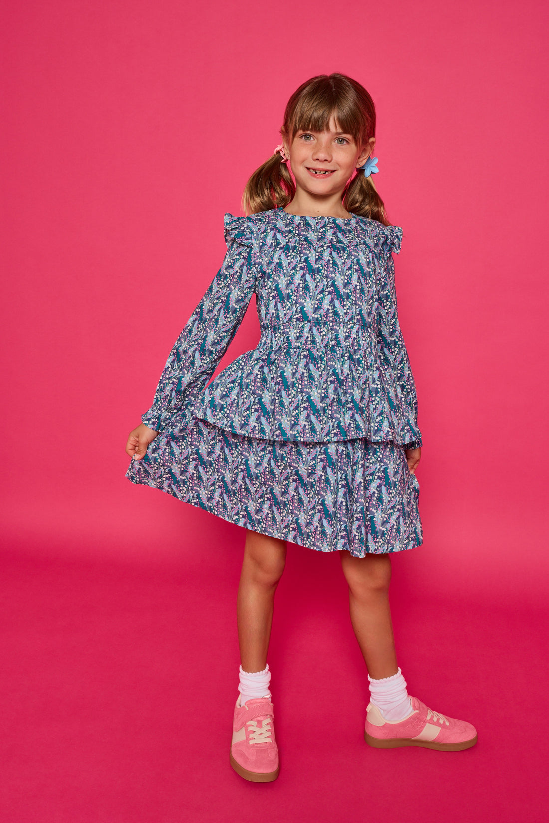 Model can be seen wearing a long sleeve woven dress in an blue/purple/white floral print. Dress features tiers, elastic ruched waistband, and angel sleeves at the top of the long sleeves for an elevated look. 