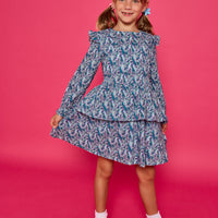 Model can be seen wearing a long sleeve woven dress in an blue/purple/white floral print. Dress features tiers, elastic ruched waistband, and angel sleeves at the top of the long sleeves for an elevated look. 