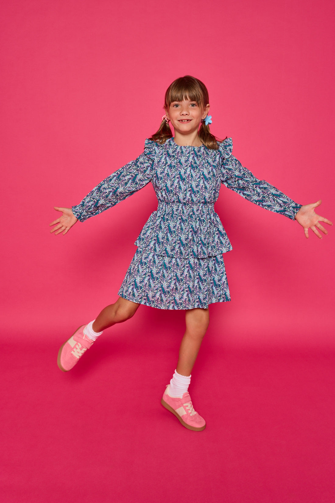 Model can be seen wearing a long sleeve woven dress in an blue/purple/white floral print. Dress features tiers, elastic ruched waistband, and angel sleeves at the top of the long sleeves for an elevated look. 