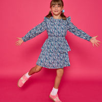Model can be seen wearing a long sleeve woven dress in an blue/purple/white floral print. Dress features tiers, elastic ruched waistband, and angel sleeves at the top of the long sleeves for an elevated look. 