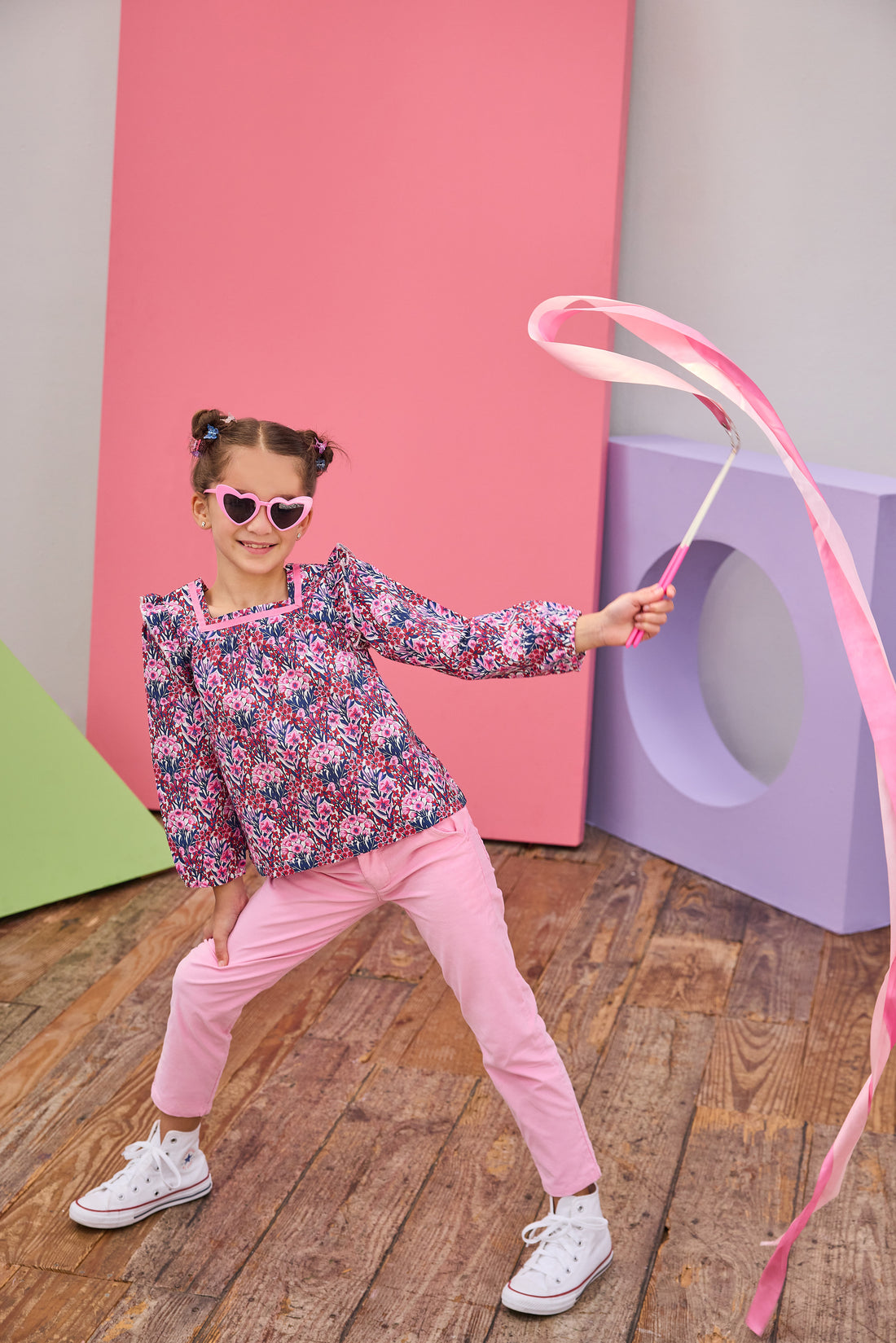 Model can be seen wearing a woven long sleeve top in a navy/pink/red floral print, paired back with bubblegum pink pants . Top features a square neckline, with a ribbon detail along neckline and slight angel sleeves to elevate the look. 