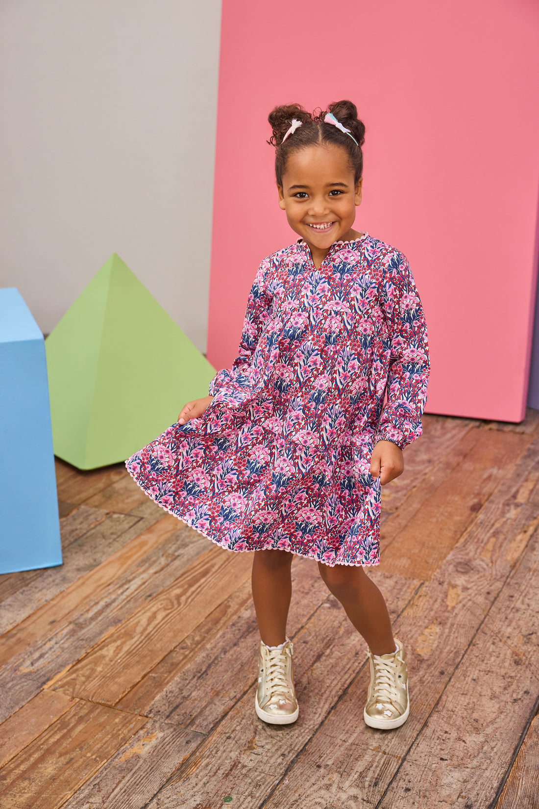 Model can be seen wearing long sleeve woven dress in a beautiful navy/pink/cranberry floral print. Dress features a beautiful light pink ric rac detail along neckline and bottom tier of dress and also features button closure along back for easy put on access. 