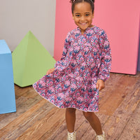 Model can be seen wearing long sleeve woven dress in a beautiful navy/pink/cranberry floral print. Dress features a beautiful light pink ric rac detail along neckline and bottom tier of dress and also features button closure along back for easy put on access. 