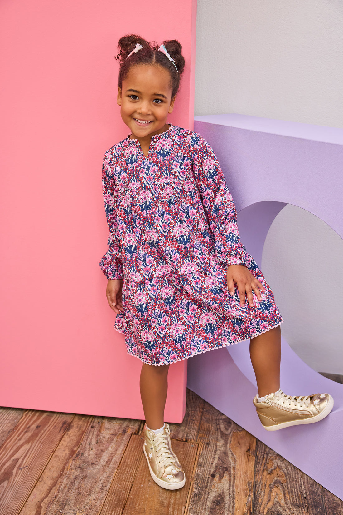 Model can be seen wearing long sleeve woven dress in a beautiful navy/pink/cranberry floral print. Dress features a beautiful light pink ric rac detail along neckline and bottom tier of dress and also features button closure along back for easy put on access. 