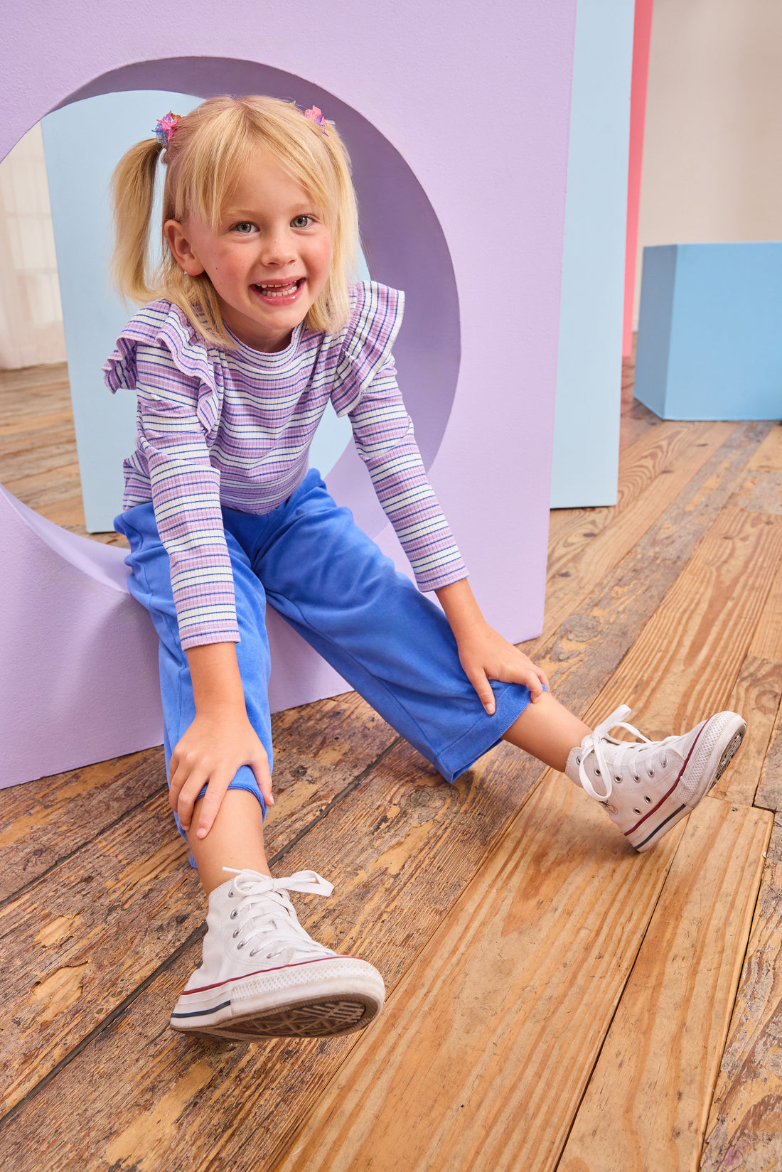 Model can be seen wearing royal blue velour pants that feature an elastic waistband and functioning pockets in the front of pants. Pants pair pack perfectly with long sleeve knit top in purple and matching blue stripe to complete the look. 