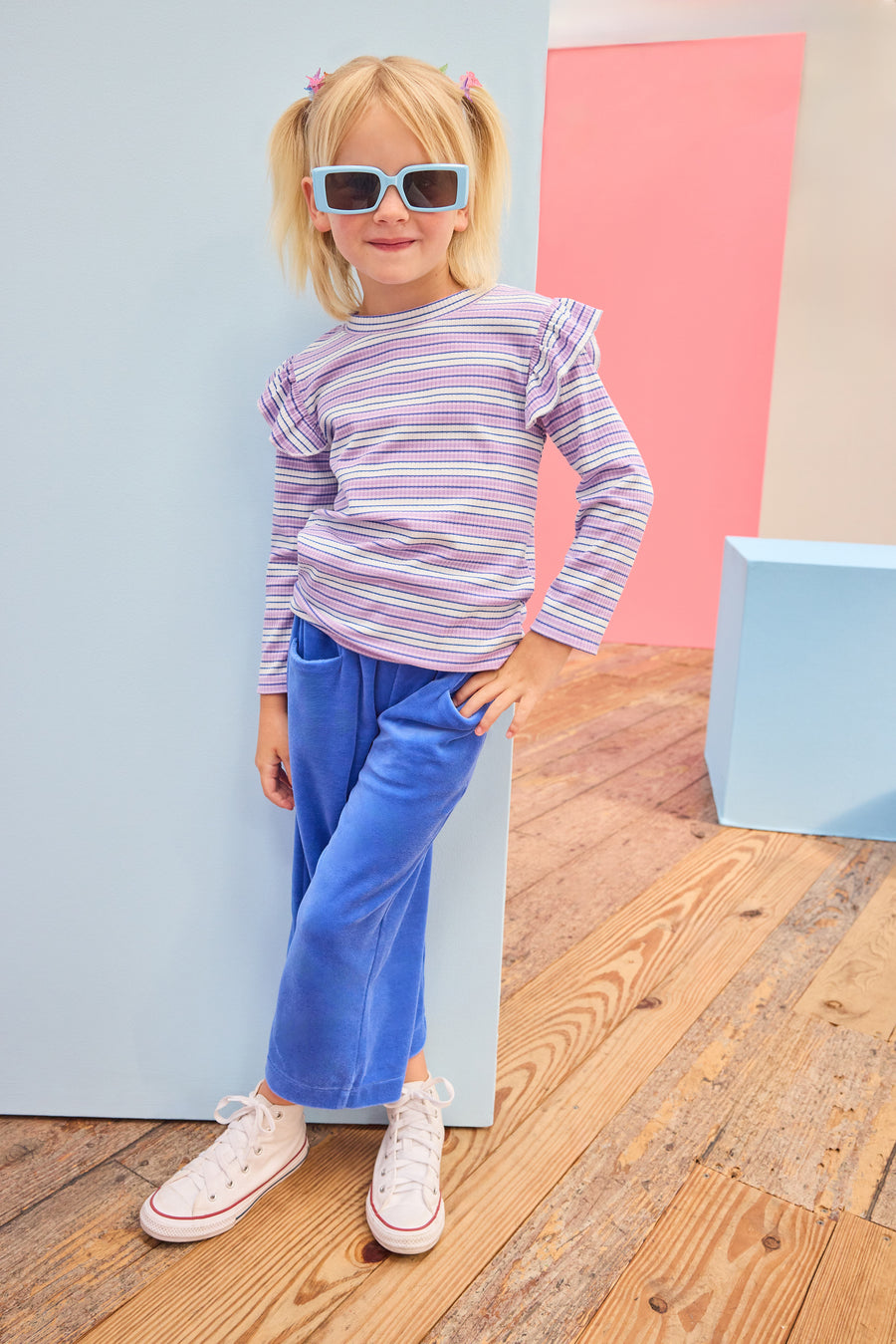 Model can be seen wearing knit ribbed stripe shirt in a fun purple/blue/white stripe that features angel sleeve detail at top of sleeves. Top pairs back perfectly with knit velour pants in royal blue to complete the look. 