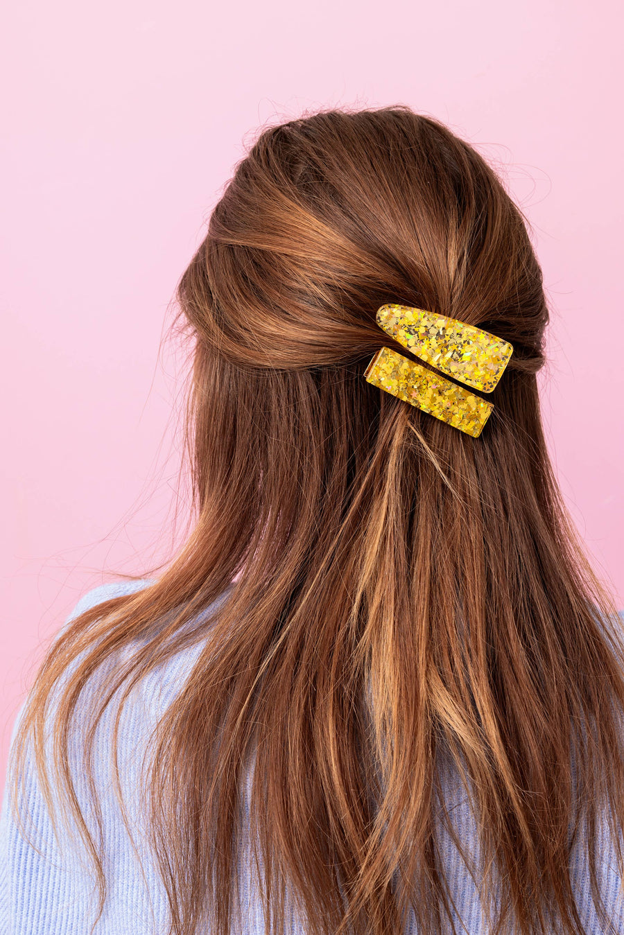 Long brown hair with a yellow hair clip against a pink background
