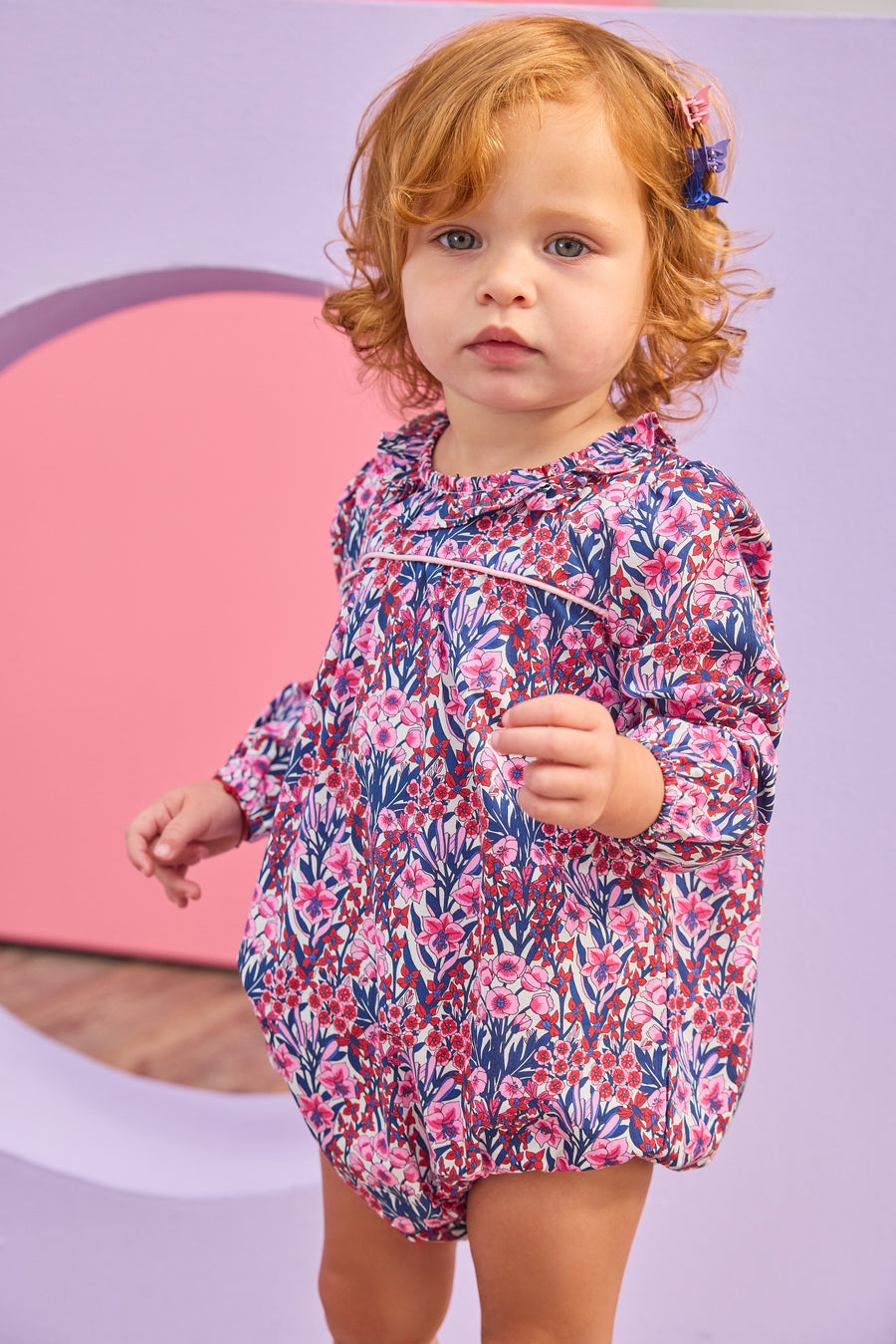 Baby girl can be seen wearing a woven bubble in a gorgeous pink/navy/cranberry color floral that features a ruffle neckline and snap closure for easy put on/pull off access. 