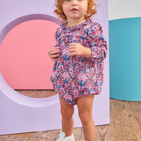 Baby girl can be seen wearing a woven bubble in a gorgeous pink/navy/cranberry color floral that features a ruffle neckline and snap closure for easy put on/pull off access. 