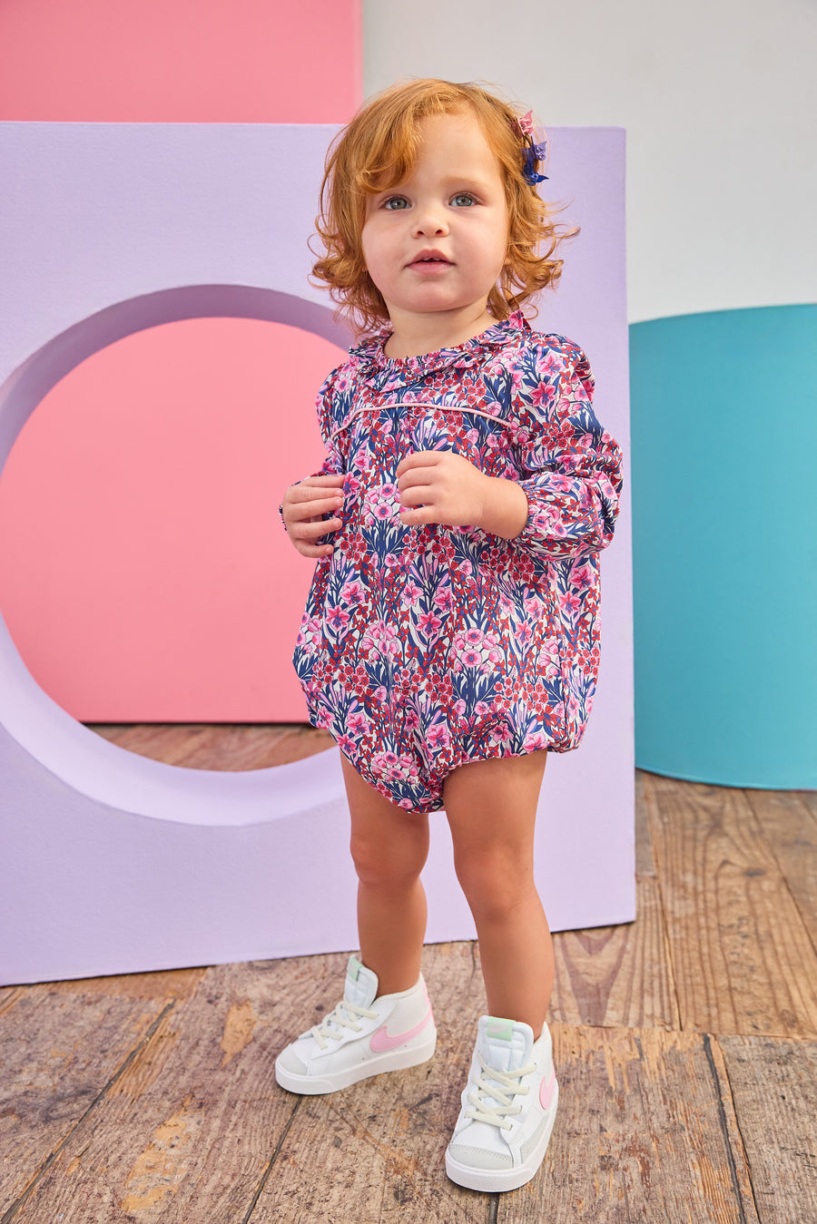 Baby girl can be seen wearing a woven bubble in a gorgeous pink/navy/cranberry color floral that features a ruffle neckline and snap closure for easy put on/pull off access. 