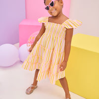 Model can be seen wearing a woven dress in a yellow/pink seersucker fabric. Dress features smocking detail across bust and slight angel sleeves to elevate the look. 