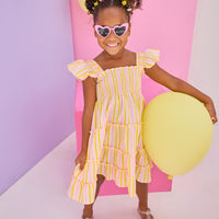 Model can be seen wearing a woven dress in a yellow/pink seersucker fabric. Dress features smocking detail across bust and slight angel sleeves to elevate the look. 