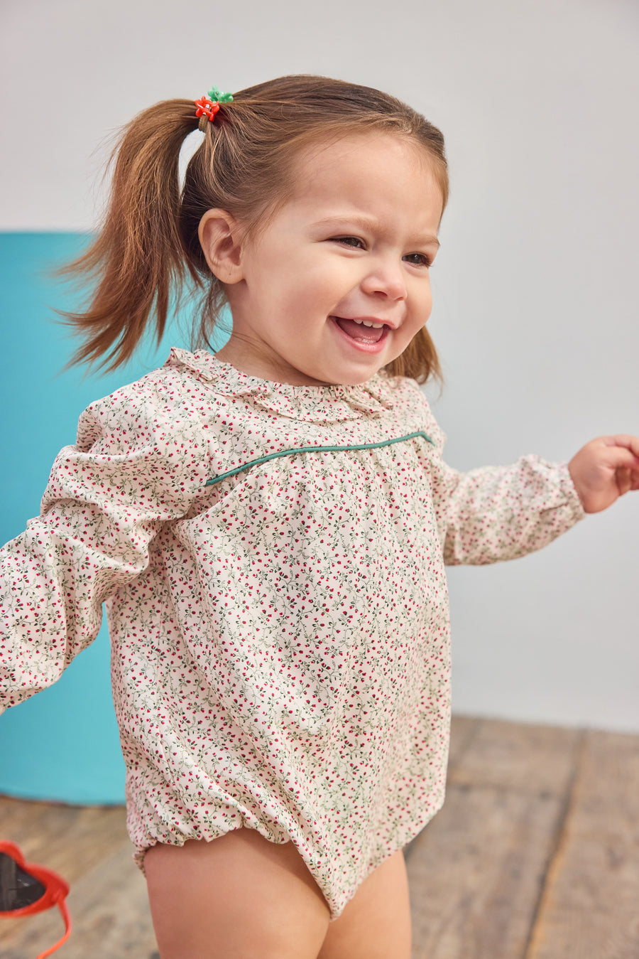 Baby girl can be seen wearing a woven bubble in a gorgeous red and green color floral that features a ruffle neckline and snap closure for easy put on/pull off access. 