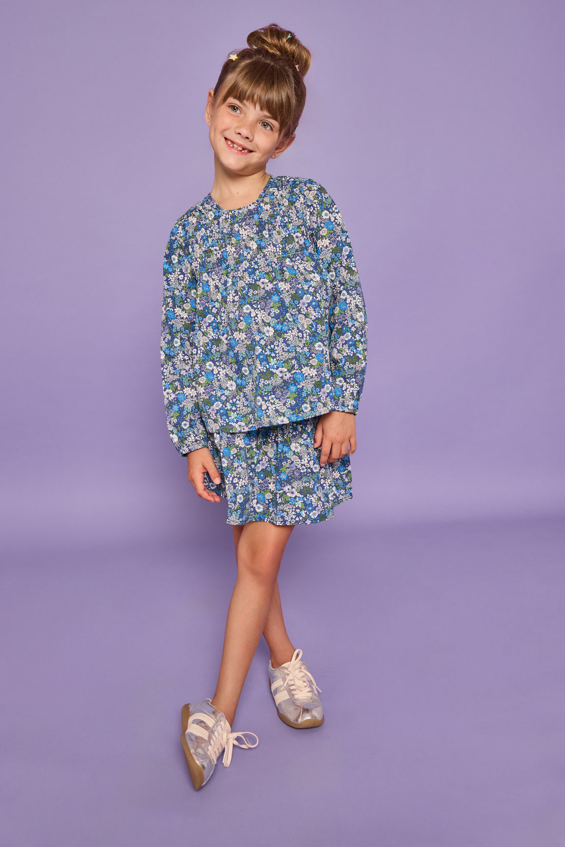 Model can be seen wearing a long sleeve woven dress in a blue/purple/white floral print. Top features ruching across the bust and elastic at the sleeves. 