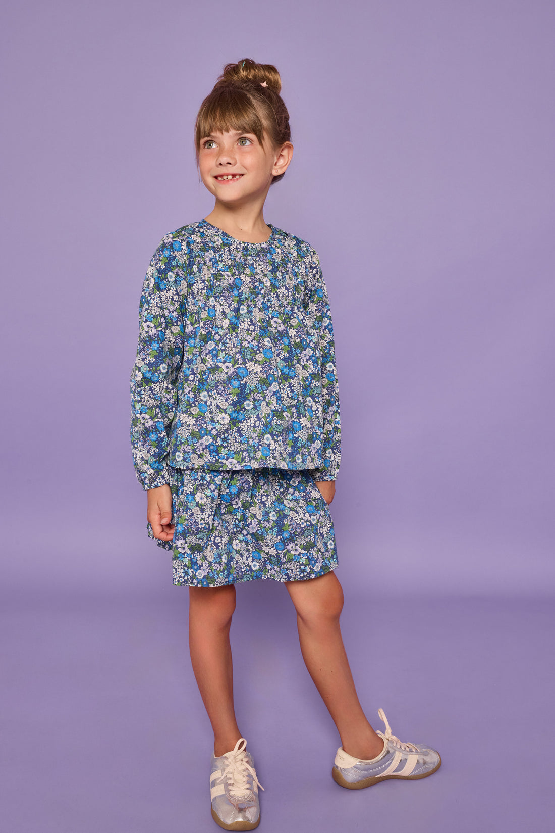 Model can be seen wearing a long sleeve woven dress in a blue/purple/white floral print. Top features ruching across the bust and elastic at the sleeves. 