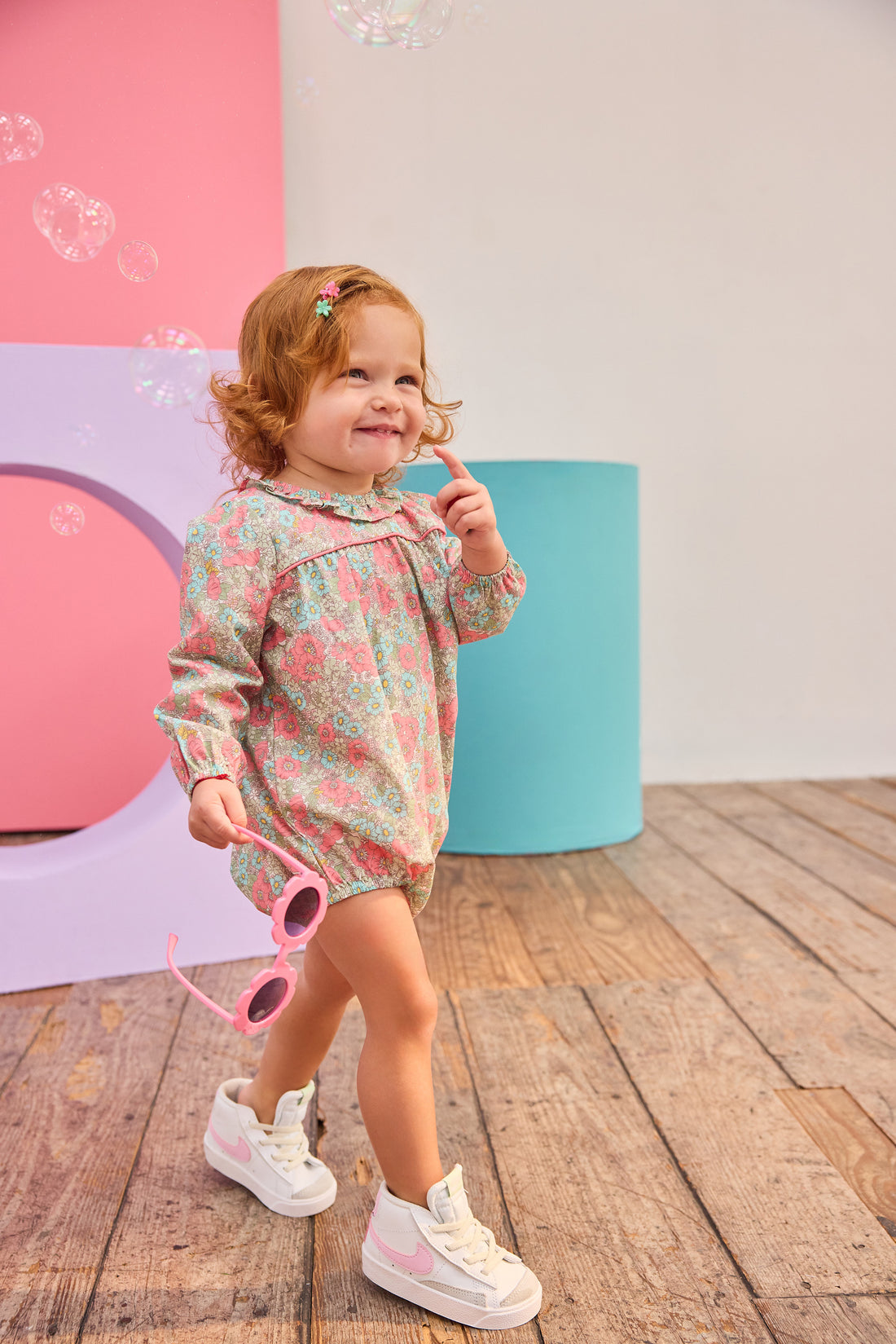 Baby girl can be seen wearing a woven bubble in a gorgeous pink/teal floral that features a ruffle neckline and snap closure for easy put on/pull off access. 