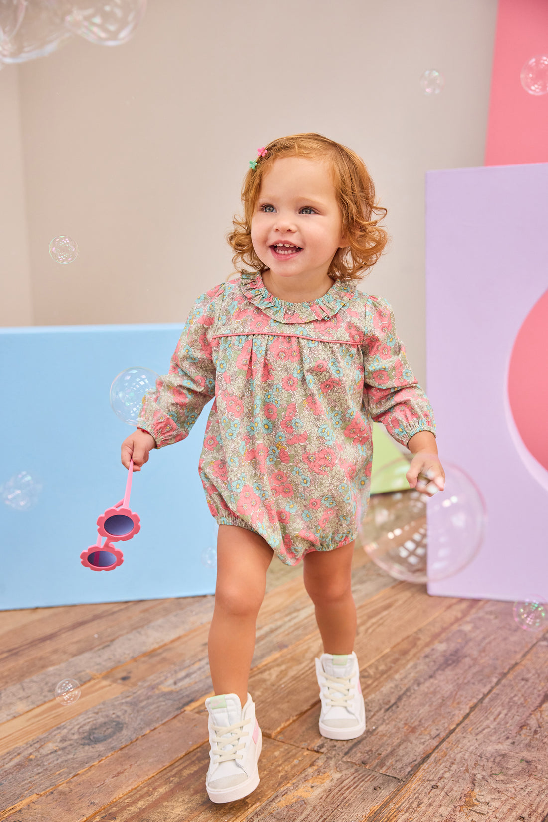 Baby girl can be seen wearing a woven bubble in a gorgeous pink/teal floral that features a ruffle neckline and snap closure for easy put on/pull off access. 