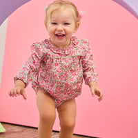 Baby girl can be seen wearing a pink/green floral woven bubble that features  a stunning ruffled collar and ¾ length sleeves. The bubble also has snap closures at the stride, and buttons on back for easy pull on/take off access. 