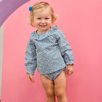 Baby model can be seen wearing a woven bloomer set in a blue floral print that features two  button closure on front of top of the set at neckline and elastic waist on bottoms for easy put on/take off access. 