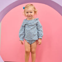 Baby model can be seen wearing a woven bloomer set in a blue floral print that features two  button closure on front of top of the set at neckline and elastic waist on bottoms for easy put on/take off access. 