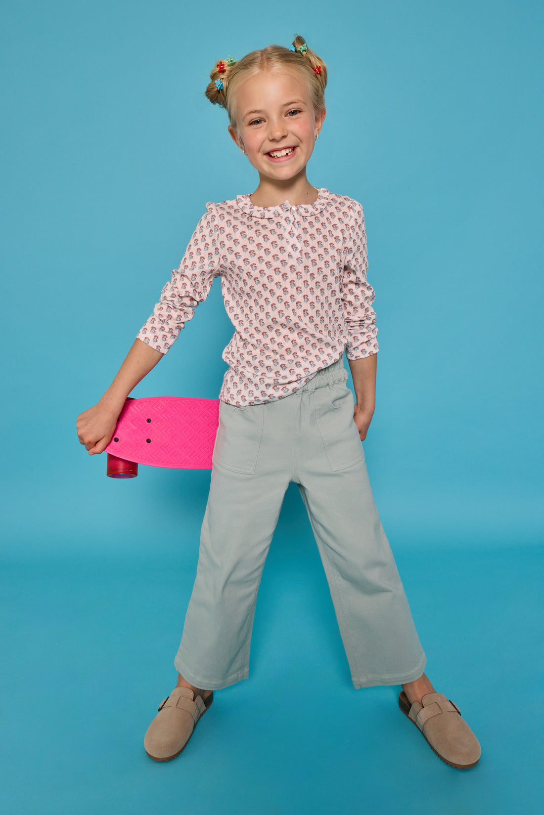 Model can be seen wearing a long sleeve knit tee in an orange/green floral print. Top features three button closure at neckline and a ruffle collar for an elevated look. Top pairs back perfectly with our light green pants that feature two pockets and elastic waistband for easy pull on access. 