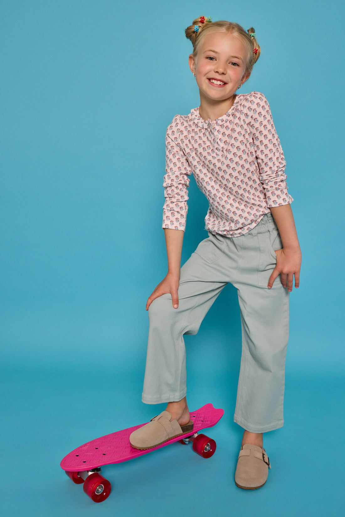 Model can be seen wearing a long sleeve knit tee in an orange/green floral print. Top features three button closure at neckline and a ruffle collar for an elevated look. Top pairs back perfectly with our light green pants that feature two pockets and elastic waistband for easy pull on access. 