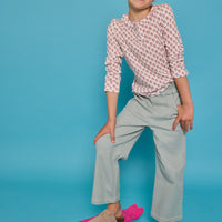 Model can be seen wearing a long sleeve knit tee in an orange/green floral print. Top features three button closure at neckline and a ruffle collar for an elevated look. Top pairs back perfectly with our light green pants that feature two pockets and elastic waistband for easy pull on access. 