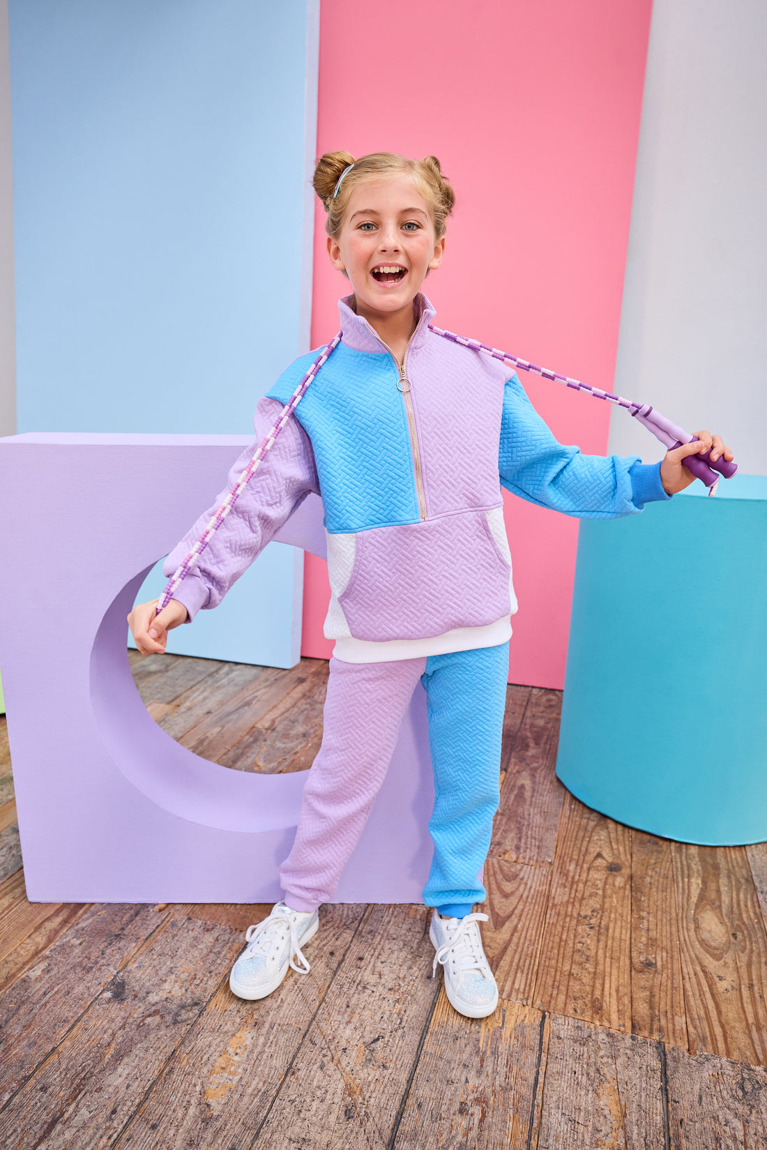 Model can be seen wearing a matching color block set in purple/aqua/and white. Pullover features a gold quarter zip zipper detail and large front pocket for a relaxed but secure fit. Pullover matches back perfectly to the joggers, and continues with the color block with a purple pant leg and an aqua pant leg.