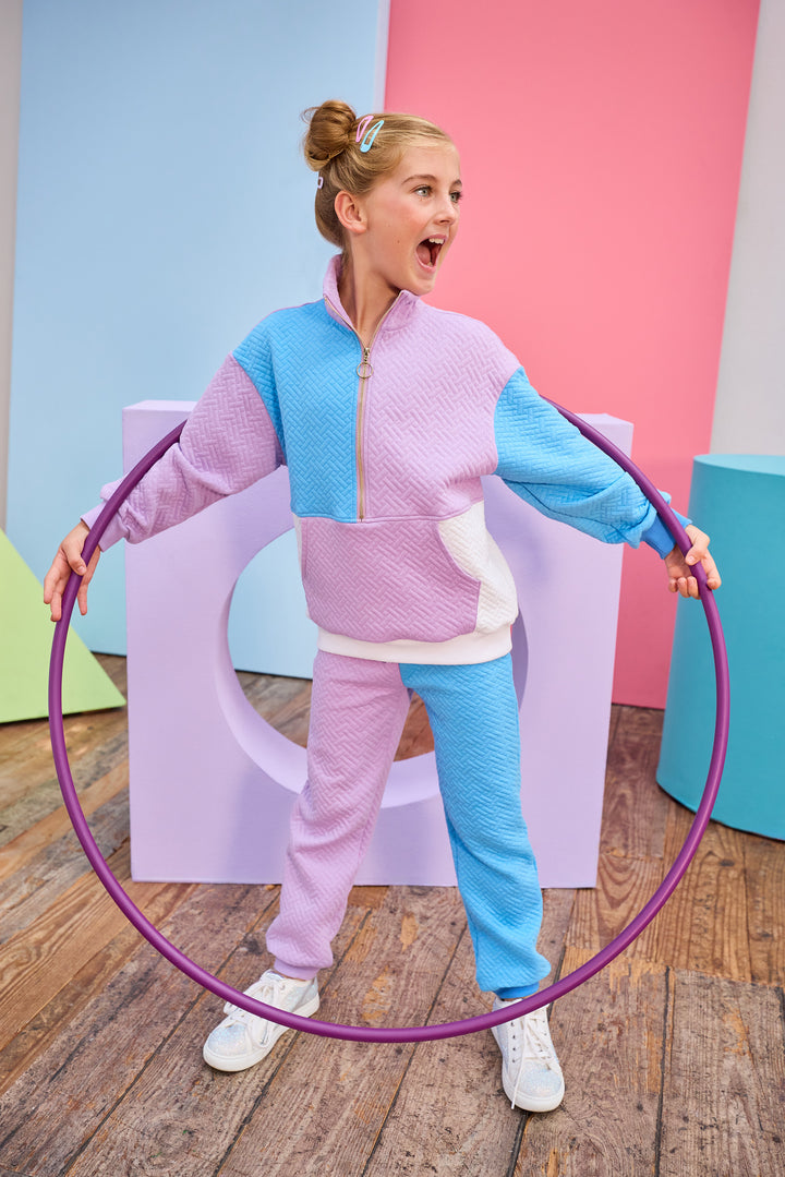 Model can be seen wearing a matching color block set in purple/aqua/and white. Pullover features a gold quarter zip zipper detail and large front pocket for a relaxed but secure fit. Pullover matches back perfectly to the joggers, and continues with the color block with a purple pant leg and an aqua pant leg.