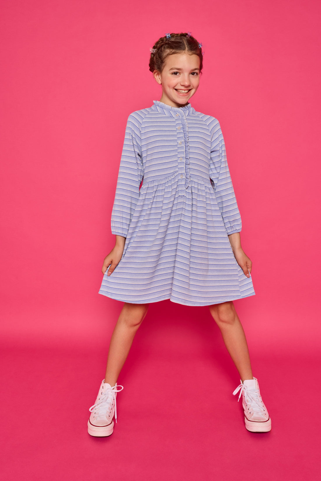 Model can be seen wearing a long sleeved knit dress in a sparkly blue and white stripe fabric. Dress features button closure down the front for a relaxed but secure fit. 