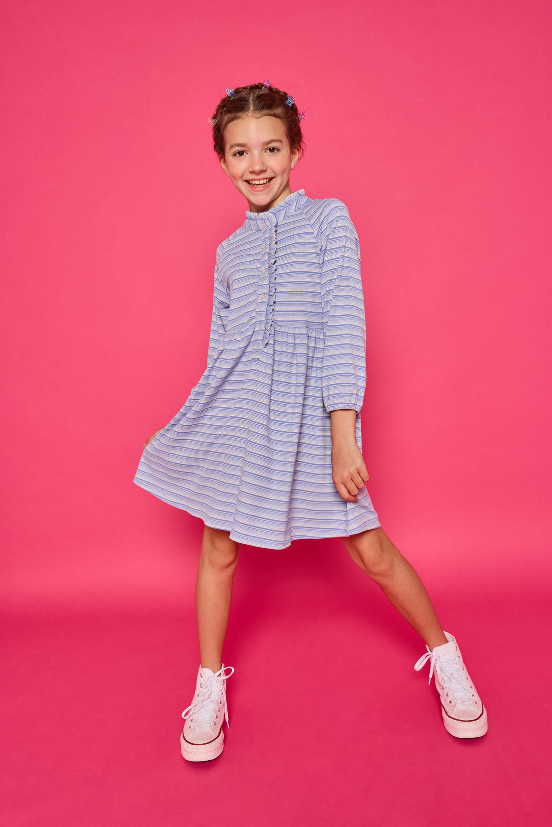 Model can be seen wearing a long sleeved knit dress in a sparkly blue and white stripe fabric. Dress features button closure down the front for a relaxed but secure fit. 