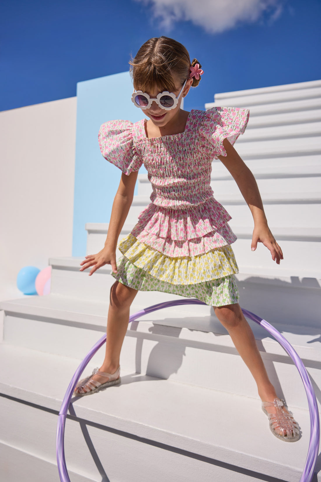 Model can be seen wearing woven pink floral print top that features elastic smocking throughout the body of the top for a stretchy but secure fit. Top pairs back perfectly with three tiered skort in matching floral print in pink/yellow/green floral tiers. 