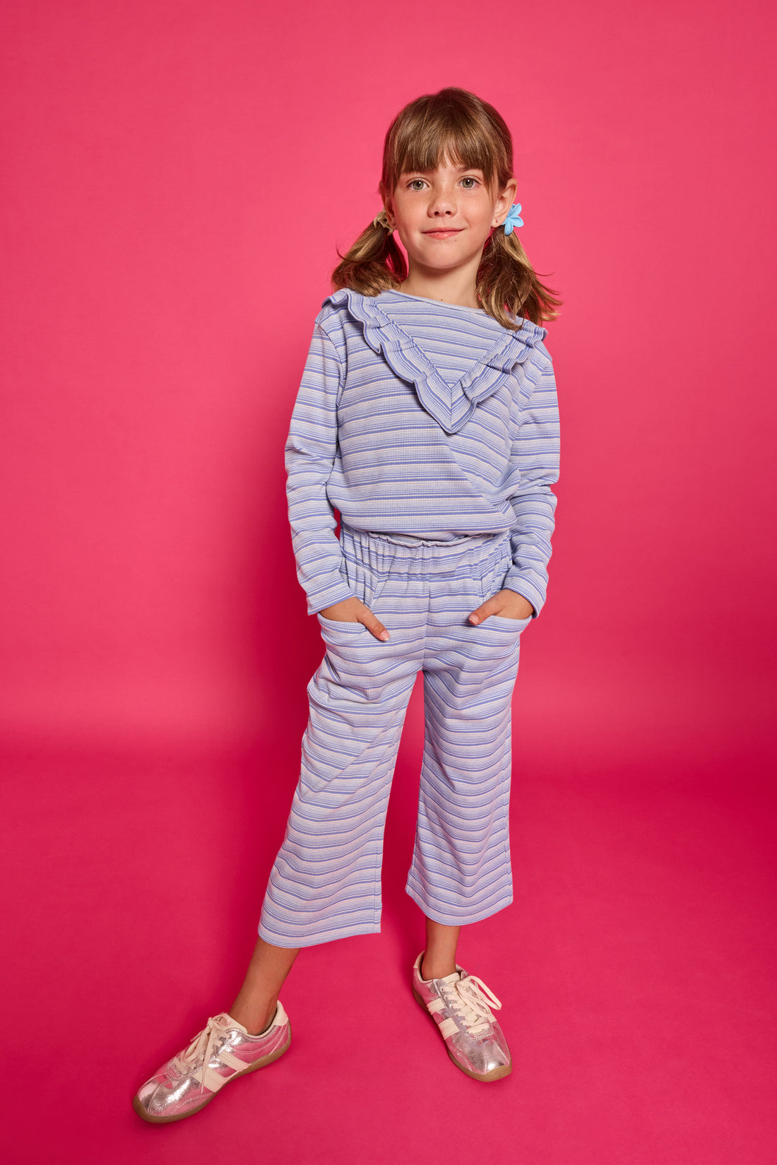 Model can be seen wearing a blue/white/sparkle striped long sleeve knit shirt. Shirt features a v-ruffle detail across bust for an elevated look. 