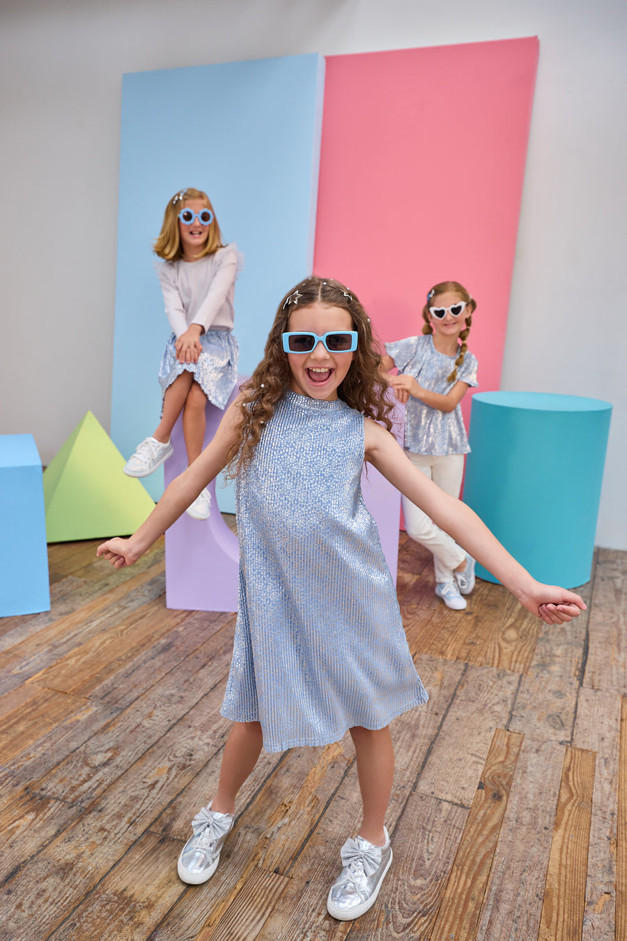 Children posing in front of colorful geometric shapes on a wooden floor in matching outfits.