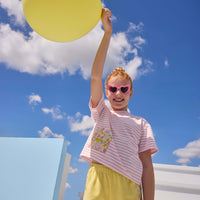 Model can be seen wearing yellow knit shorts that feature an elastic waistband and woven pink/yellow floral trim detail along bottom and sides of shorts to elevate the look. Shorts pair back perfectly with pink/white knit striped t-shirt that has a pocket detail in the same floral print to pair back with the shorts. 
