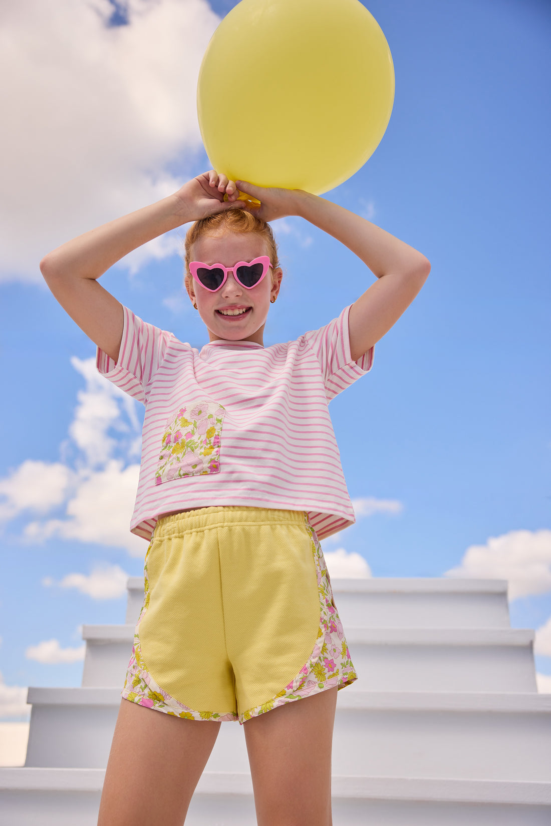 Model can be seen wearing pink and white stripe knit boxy tee that features a floral patch pocket that matches back perfectly with the pink/yellow floral trim on the track shorts to complete the look. 