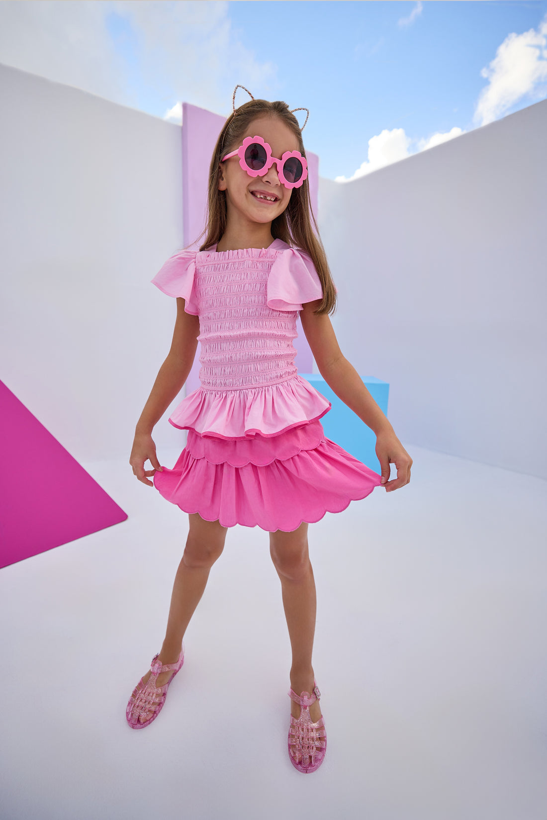 Model can be seen wearing woven hot pink two tiered skort. Skort features elastic waistband and built in shorts for a secure fit. Skort pairs back perfectly with woven smocked top in light pink with hot pink bottom trim to complete the look. 