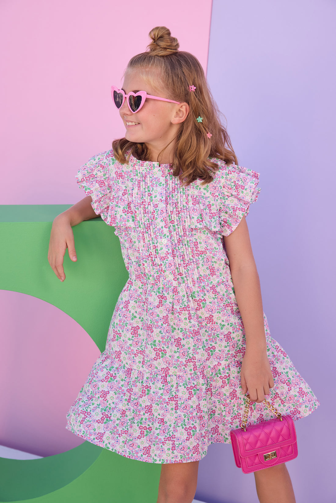 Model can be seen wearing a woven dress in a pink/green floral print. Dress features angel sleeves, button closure down the front, and tier details to elevate the look. 