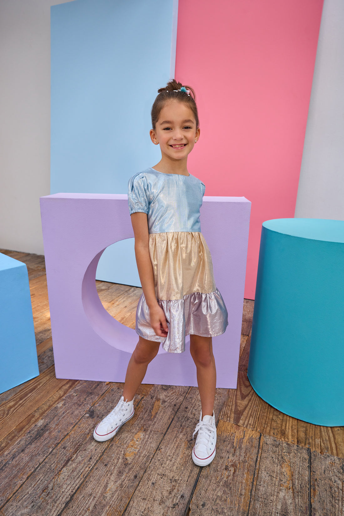 Tween model can be seen wearing a metallic dress that has an ice blue metallic top, gold metallic waist, and purple metallic bottom tier for a fun elevated look. 