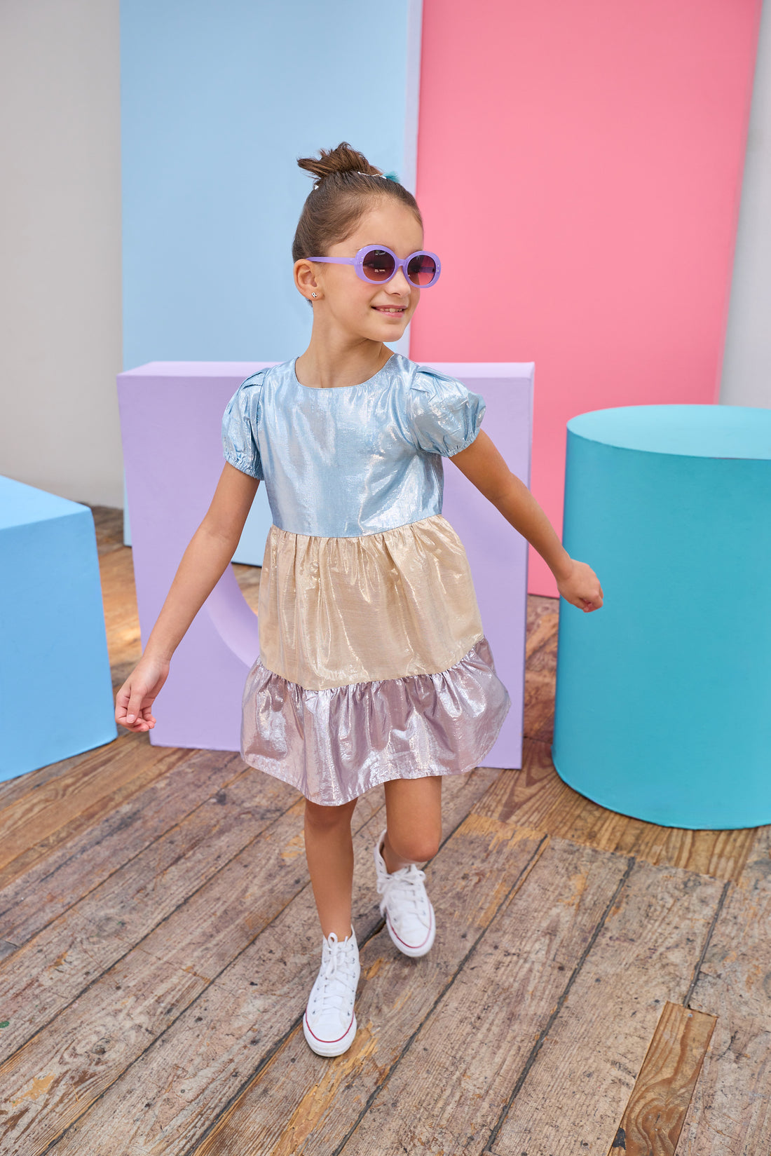 Tween model can be seen wearing a metallic dress that has an ice blue metallic top, gold metallic waist, and purple metallic bottom tier for a fun elevated look. 